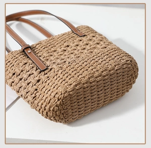 Close-up of woven straw tote bag featuring brown leather handles and silver rivet details