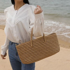 Handmade woven straw tote bag for beach vacation held by a model on a sandy coast