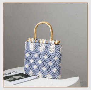 Detail of blue and white diamond woven cotton bag with curved bamboo handles on white table