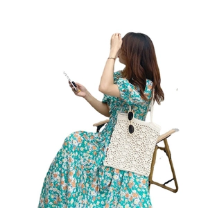 Sac à bandoulière en paille crochetée avec robe à fleurs verte sur une chaise pliante
