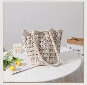 Close-up of cream handmade crochet bucket bag featuring shell stitch pattern on a lace table