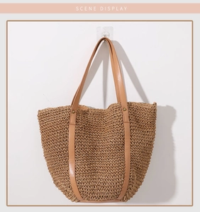 Detail of handwoven straw tote bag with brown synthetic leather handles and metal rivets