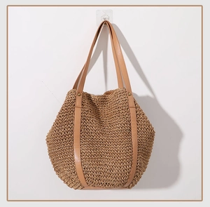 Detail of woven straw tote bag featuring brown leather handles and decorative rivets