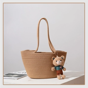 Detail of a brown woven straw tote bag with a cute teddy bear charm on white surface