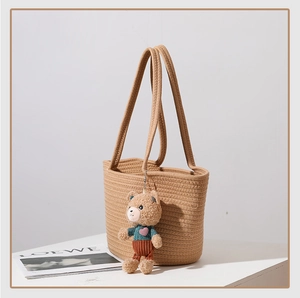 Detail of hand-woven cotton shoulder bag with a cute teddy bear pendant on white table