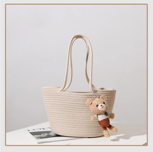 Detail shot of beige woven cotton shoulder bag featuring a cute plush bear pendant accessory
