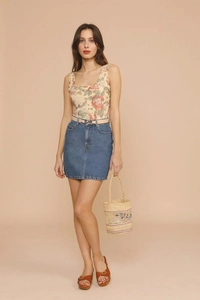 Full view of floral tank top and denim skirt paired with a cylindrical raffia beach bag