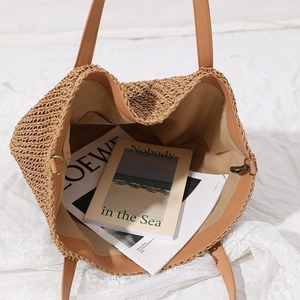 Large woven straw tote bag with brown leather handles and spacious interior for beach