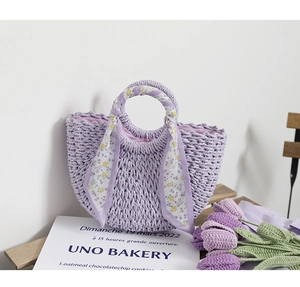 Detail of a purple woven straw bag with floral scarf handle on a wooden chair