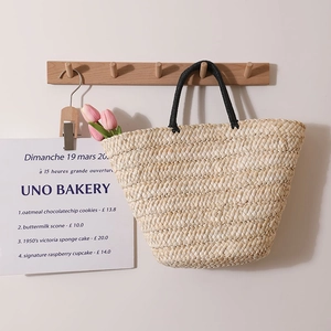 Minimalist straw tote bag with black round handles and pink tulips in home setting