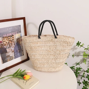 Large hand-woven straw tote bag with black handles on a table with tulips