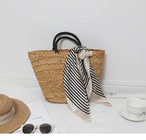 Detail of straw tote bag with black round handles and striped scarf in a beach setting