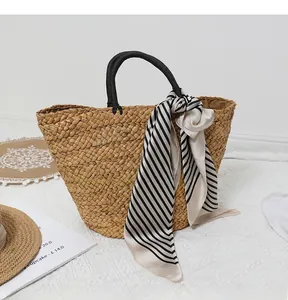 Detail of hand-woven straw beach tote with black handles and striped silk scarf