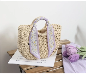 Detail of straw woven tote bag with lavender floral scarf handle on wooden bench