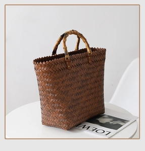 Close-up of a brown woven straw tote bag featuring natural bamboo handles on a white table