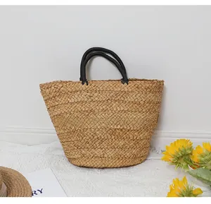 Detail of a handmade straw tote bag with black wrapped handles on a white table