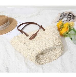 Détail d'un sac cabas en paille tressée avec poignées en cuir marron et étiquettes