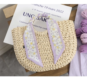 Detail of woven straw handbag featuring a purple floral silk scarf on the handle