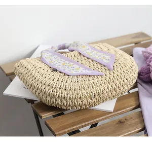 Detail of light beige straw woven handbag with elegant purple floral silk scarf on wood
