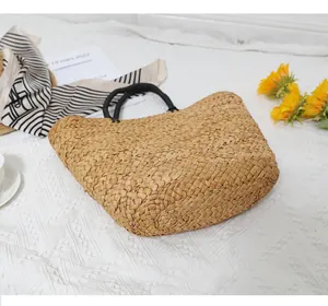 Detailed top view of large straw tote bag with black round handles on white textured blanket