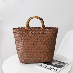 Stylish brown woven straw tote bag with bamboo top handle and minimalist design on table