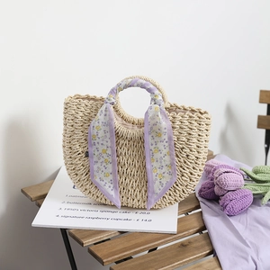 Elegant semi-circle straw woven bag with purple floral scarf handle on a wooden table