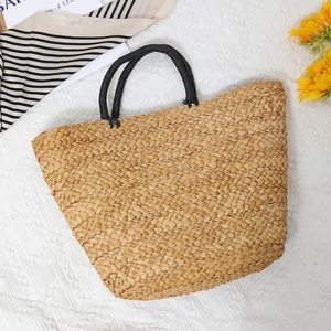 Large handmade straw tote bag with black woven handles on white lace background