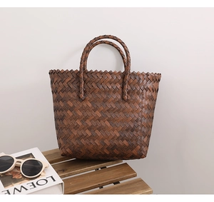 Detailed view of the woven dark brown leather tote bag on a wooden table with accessories