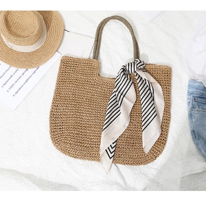 Detail of hand-woven beige straw tote bag with striped scarf on textured white fabric
