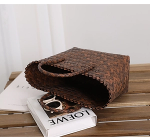 Detailed close-up of dark brown woven tote bag with intricate diagonal texture on wood