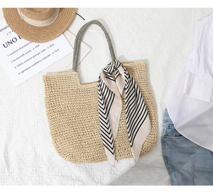Detail of hand-woven straw tote bag with black and white striped scarf on textured background