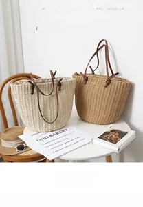 Detail of round straw bucket bags with leather handles on a white table for vacation