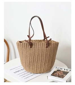 Detailed close-up of natural woven straw bucket bag with dark brown leather shoulder strap