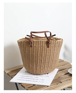 Detail of hand-woven straw bucket bag featuring brown leather handles and knot accents