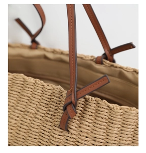 Detail of hand-woven straw tote with natural fiber texture and brown leather strap