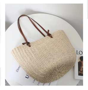 Close-up of woven straw tote bag with brown leather straps and detailed texture