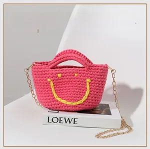 Gros plan d'un sac seau DIY en tissage rose fuchsia avec un motif smiley jaune tricoté
