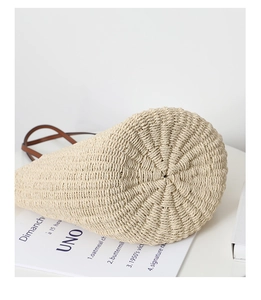Detail of hand-woven straw tote bag featuring round base and dark brown leather handle