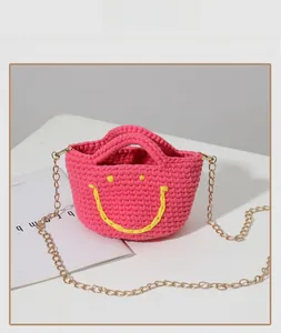 Détail du sac seau tricoté rose avec motif smiley jaune et bandoulière en chaîne dorée