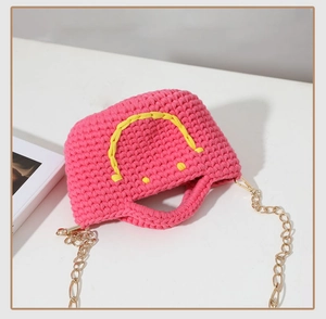 Détail du sac seau rose tricoté avec motif smiley jaune et bandoulière dorée