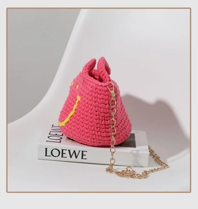Gros plan sur un sac seau rose fait main au crochet avec smiley jaune et chaîne dorée
