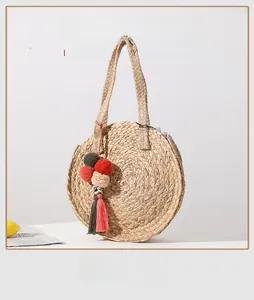Detail of round straw bag showing colorful pompom charms and natural handwoven texture