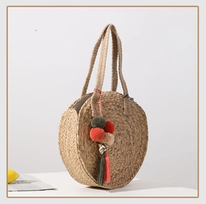 Detail view of round straw bag with colorful pom-pom tassels and shell charms