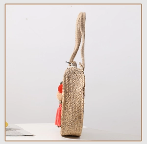 Detail view of round straw beach bag showing side thickness and colorful pompom charms