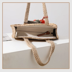 Detail of hand-woven straw tote bag with canvas lining, zipper closure and pompom charm