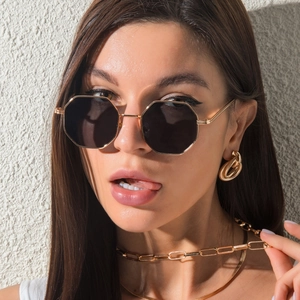 Detail of octagonal metal sunglasses with gray lenses and gold jewelry on model