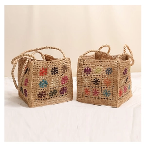 Dettaglio borsa in rafia con motivi floreali ricamati colorati e manici intrecciati