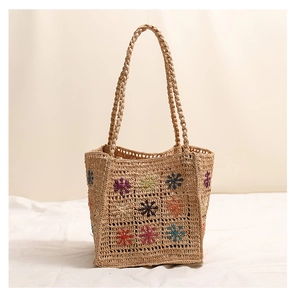 Dettaglio dei ricami floreali colorati su una borsa tote in rafia naturale intrecciata