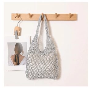 Detailed shot of silver woven hollow mesh beach bag hanging on a natural wooden hook