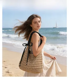 Sac bandoulière en paille avec nœud noir sur une plage ensoleillée face à la mer
